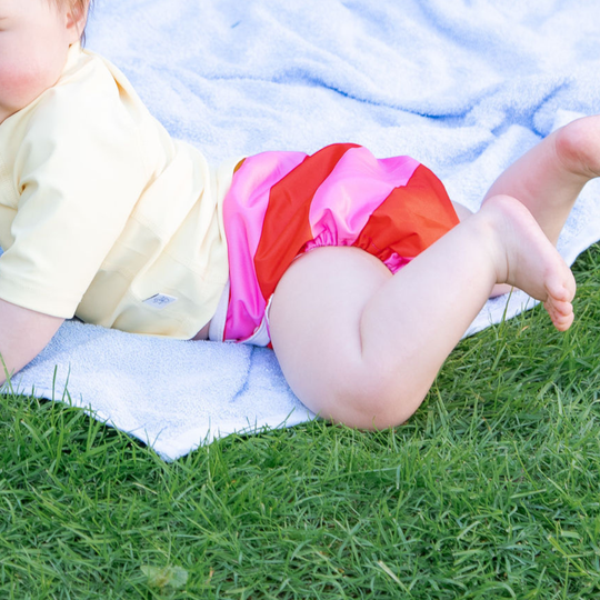Schlori Schwimmwindel Pink Stripes von Schlori-Schwimmartikel ist eine pink gestreifte Schwimmwindel mit roten Akzenten auf Gras.